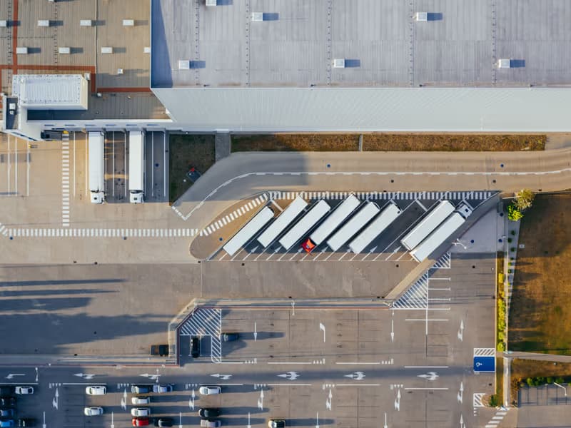 Luftbild eines Gewerbeareals mit Lastwagen an den Verladerampen und markierten Parkflächen