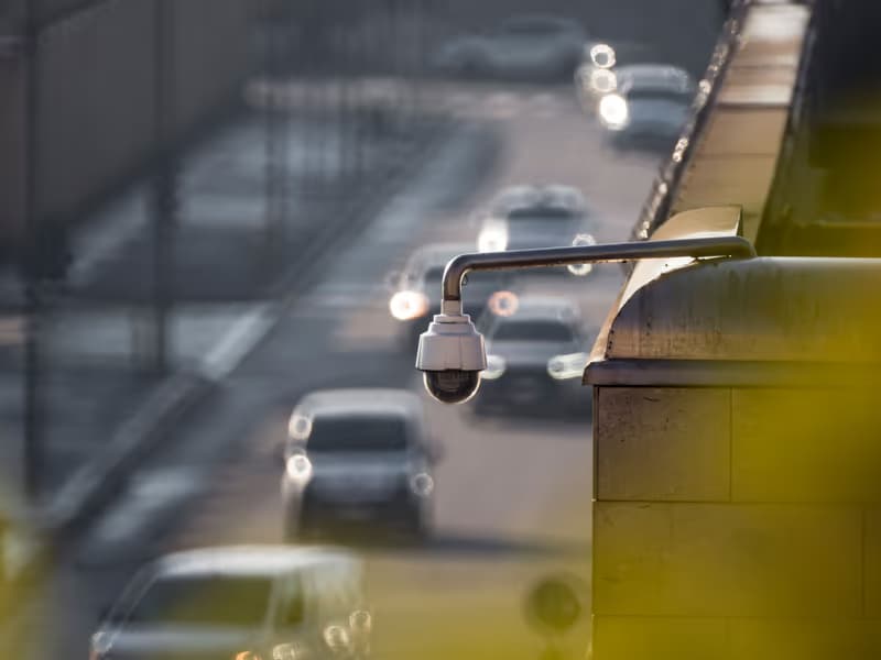 Überwachungskamera an einer Gebäudeecke über einer befahrenen Strasse