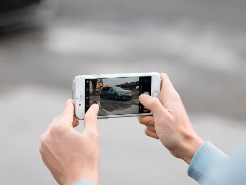 Hände halten ein Smartphone und fotografieren ein parkiertes Auto