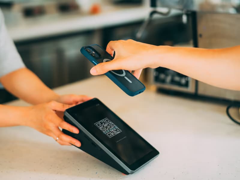 Hand hält ein Smartphone über ein Zahlterminal mit QR-Code
