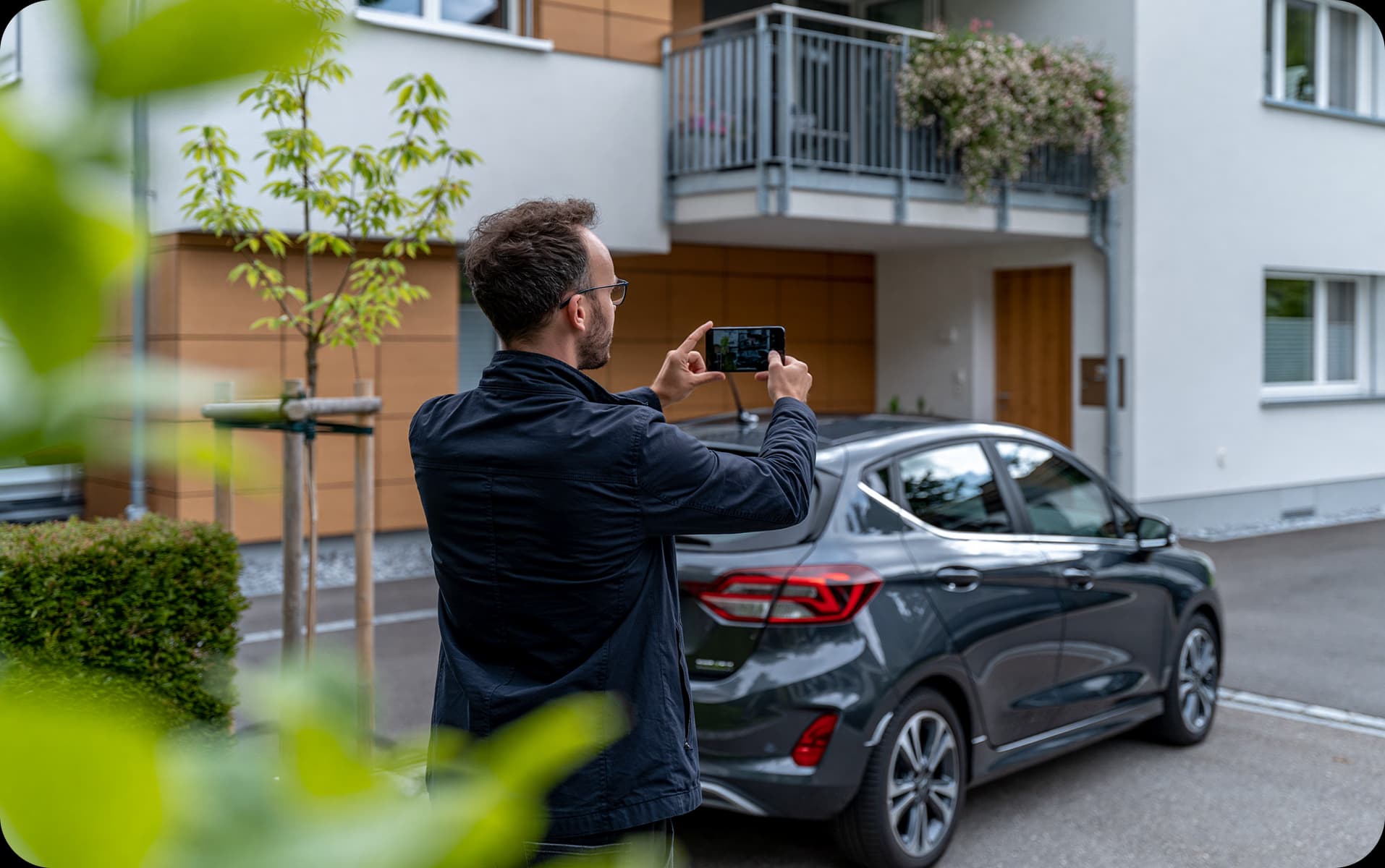 Person documenting an illegally parked car with a smartphone in front of a residential building
